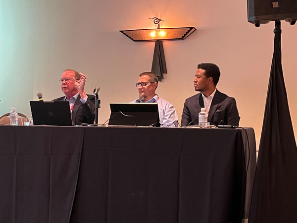 Three speakers at desk.