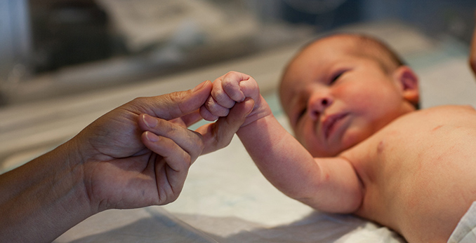 Младенец держит палец взрослого.