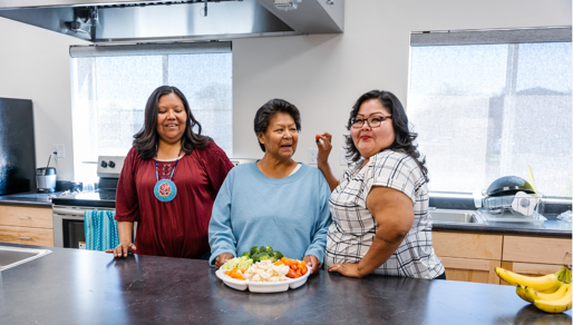 Several generations of Native American women prepare food together in a big kitchen