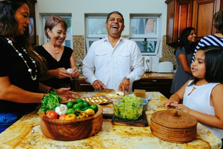Una famiglia ispanica prepara gli ingredienti attorno a un grande tavolo da pranzo