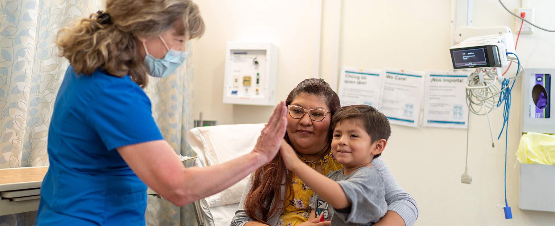 Doctor high fives a young patient sitting in his mother's lap