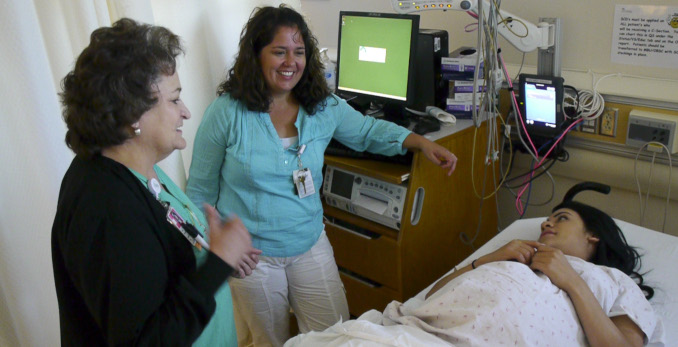 Two maternity staff members talking with pregnant woman in hospital bed.