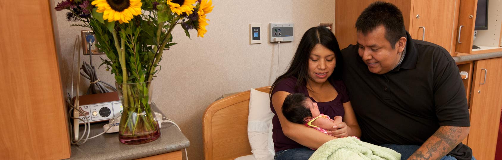 Genitori seduti nel letto d'ospedale che sorridono al neonato.
