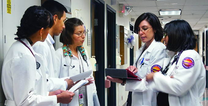 A group of care providers discuss a chart in the hallway at a hospital