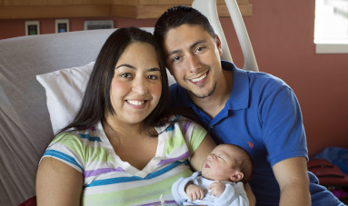 Sorrindo, mãe e pai com bebê no hospital.