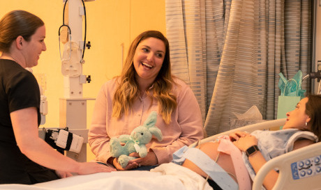 Deux femmes assises avec une femme enceinte à l'hôpital, toutes souriantes et parlant ensemble.