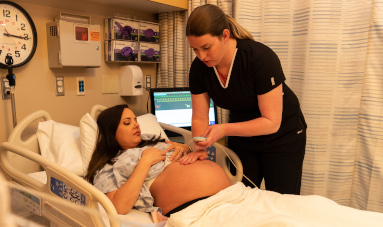 Nurse examining pregnant woman in hospital bed.