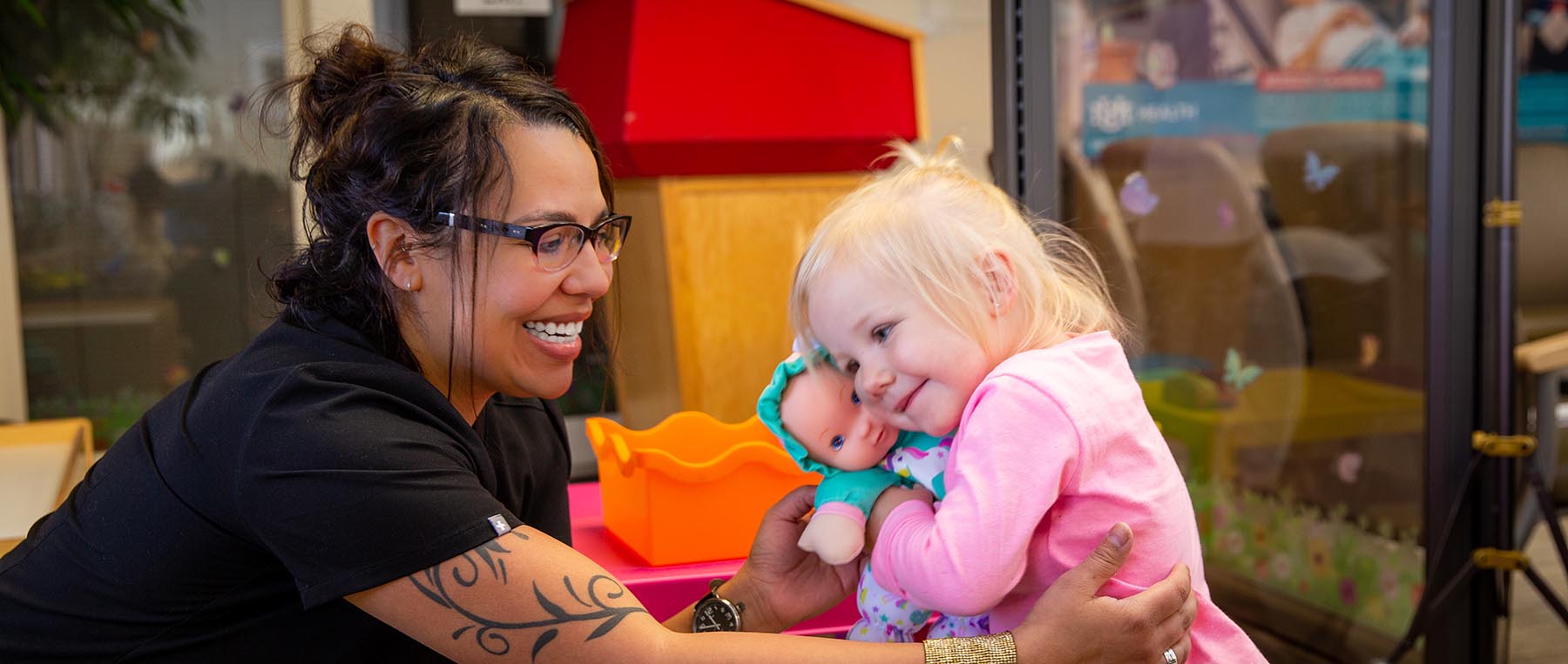 A provider smiling with a child hugging a doll