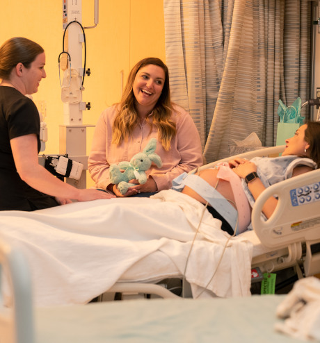 Mujeres conversando con la madre embarazada en la cama de un hospital.