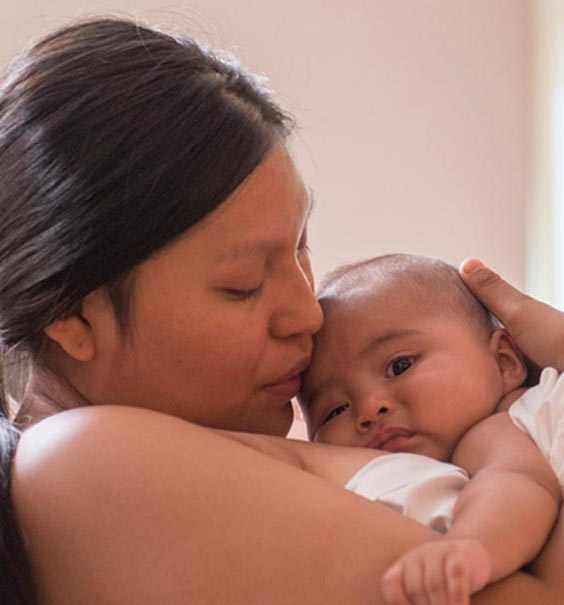 Maman dans son lit d'hôpital tenant et embrassant bébé.