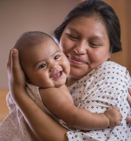 BIPOC Mamma che sorride e tiene in braccio il bambino.