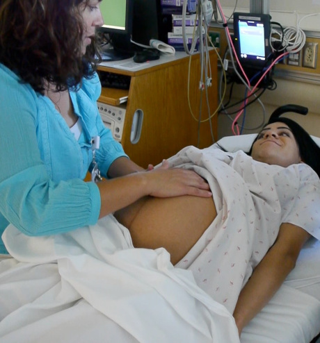 Health provider examining pregnant woman's stomach in delivery room.